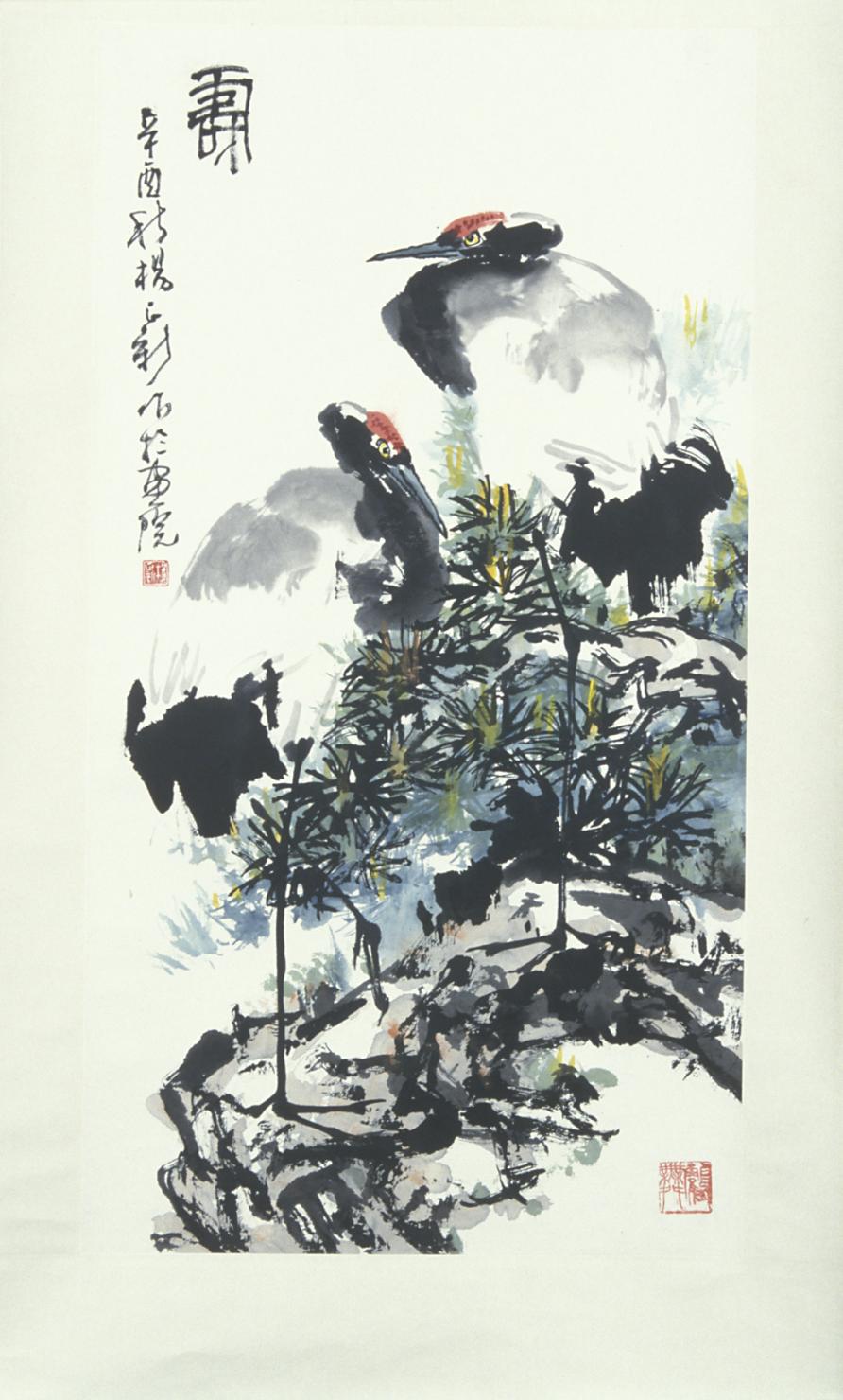 two large white cranes with black necks and a red spot on their heads stand facing each other among some scrubby trees