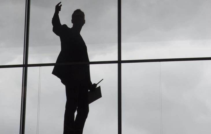 silhouette of a man standing in front of a window pointing his right hand up in the air