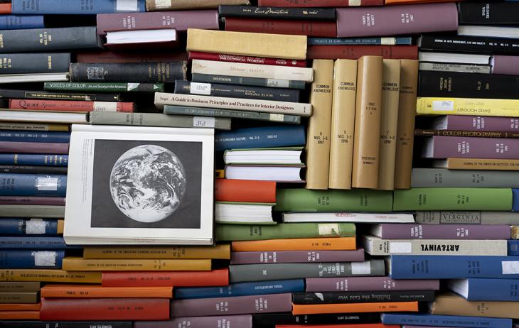 books of various sizes and colors are pilled together. One book in the center is open to a page with a black of white picture of the Earth.