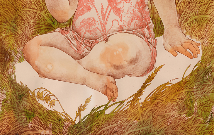 A child with light skin wearing a dress with pink plants is pictured from the chest down and sits cross-legged in a bare spot of ground surrounded by greenish-brown grasses