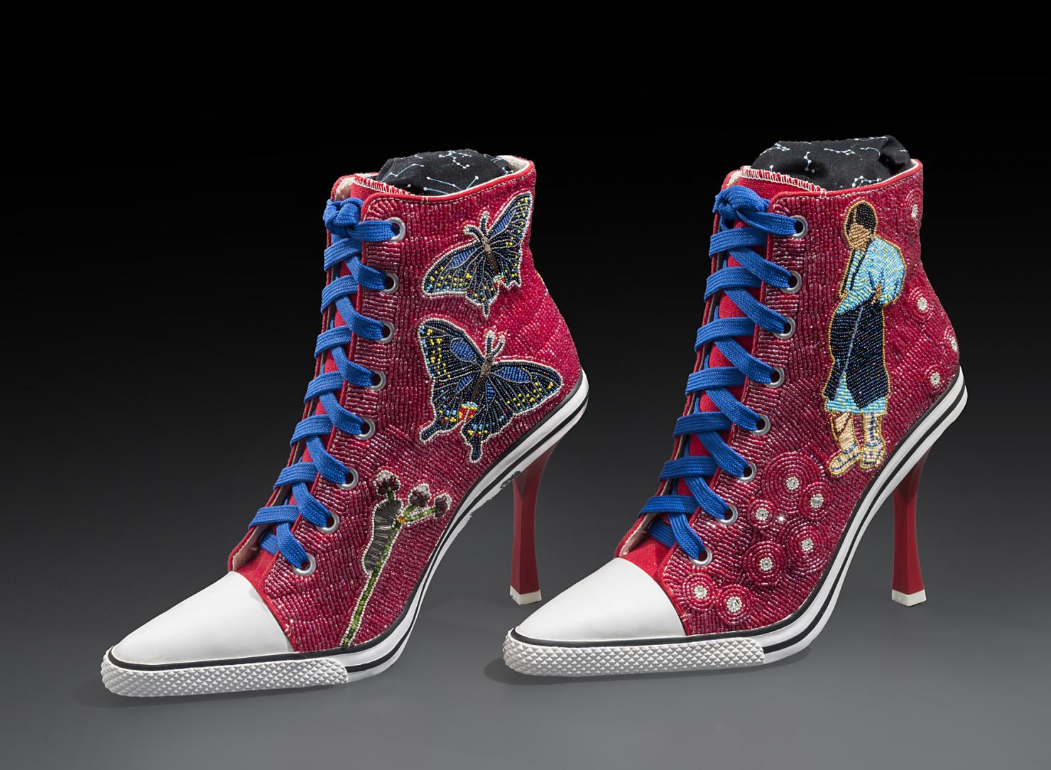 High-heeled sneakers with blue laces covered in beadwork featuring butterflies on one shoe and a pregnant woman on the other shoe