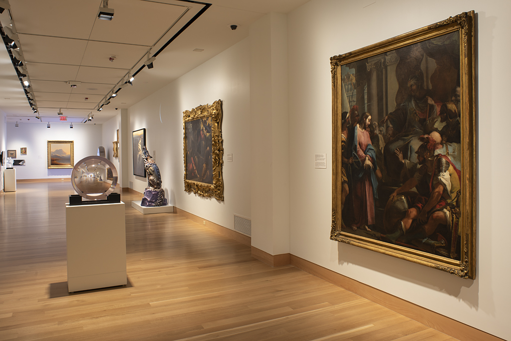 A gallery with a long wall on the right with large paintings and in the center a clear, circular sculpture