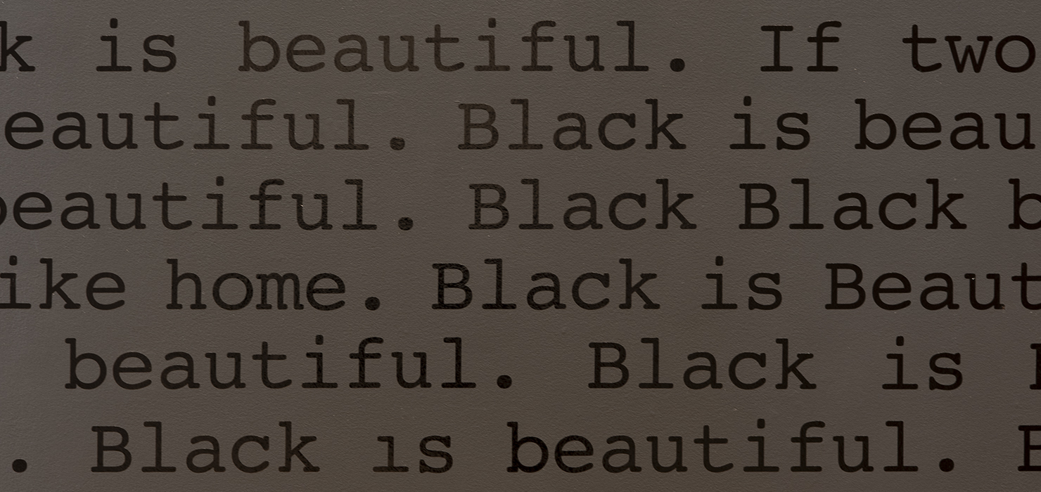 Shiny black text on a matte black wall that reads "Black is Beautiful" repeated in lines