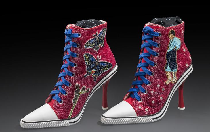 High-heeled sneakers with blue laces covered in beadwork featuring butterflies on one shoe and a pregnant woman on the other shoe