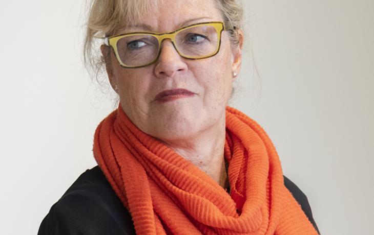 Photographic color portrait of a light-skinned woman with blonde hair, yellow glasses, and a bright orange scarf