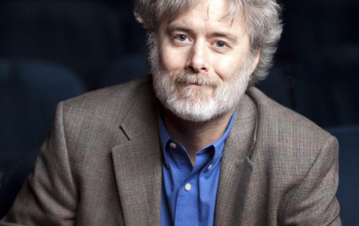 Color photograph of a man (Perry Alexander) with gray hair and a beard wearing a blue shirt and light brown suit jacket