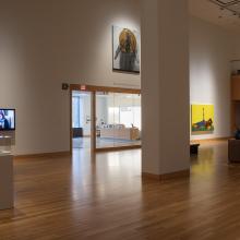 A gallery with small sculptures, a video installation, and several paintings displayed