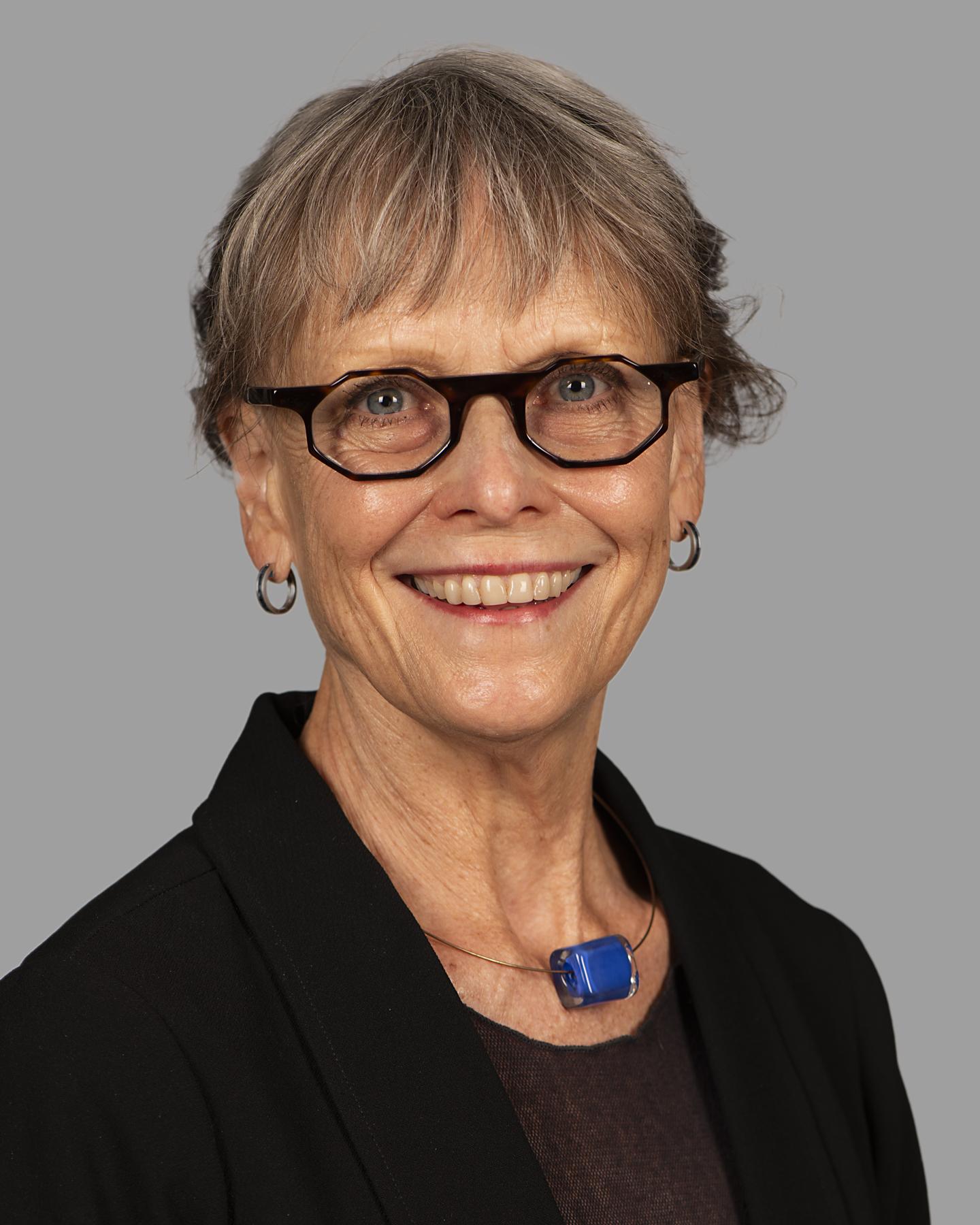 An adult woman with grey hair and glasses wearing a necklace with a large blue bead