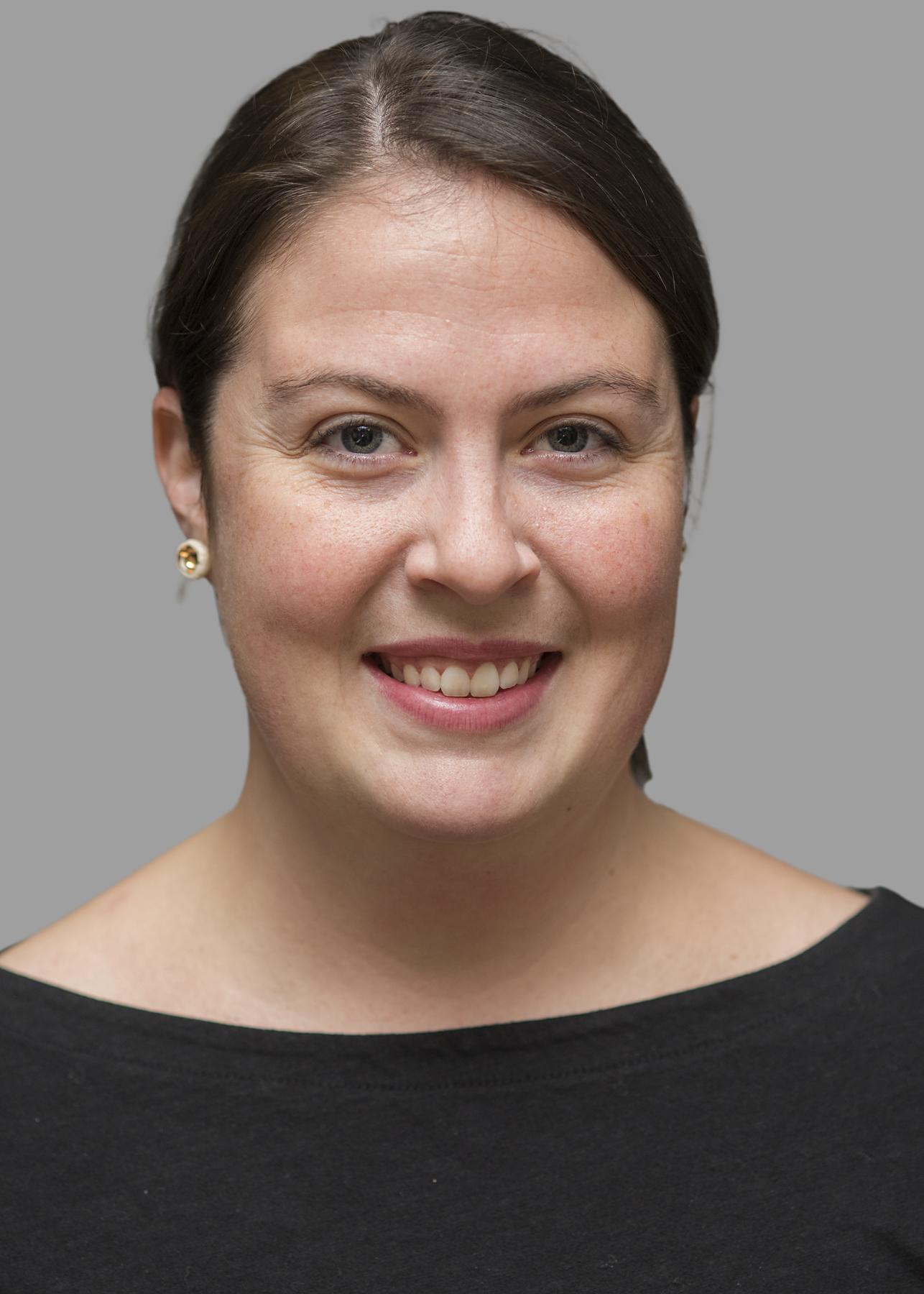 A white woman with tied back brown hair smiles at the camera