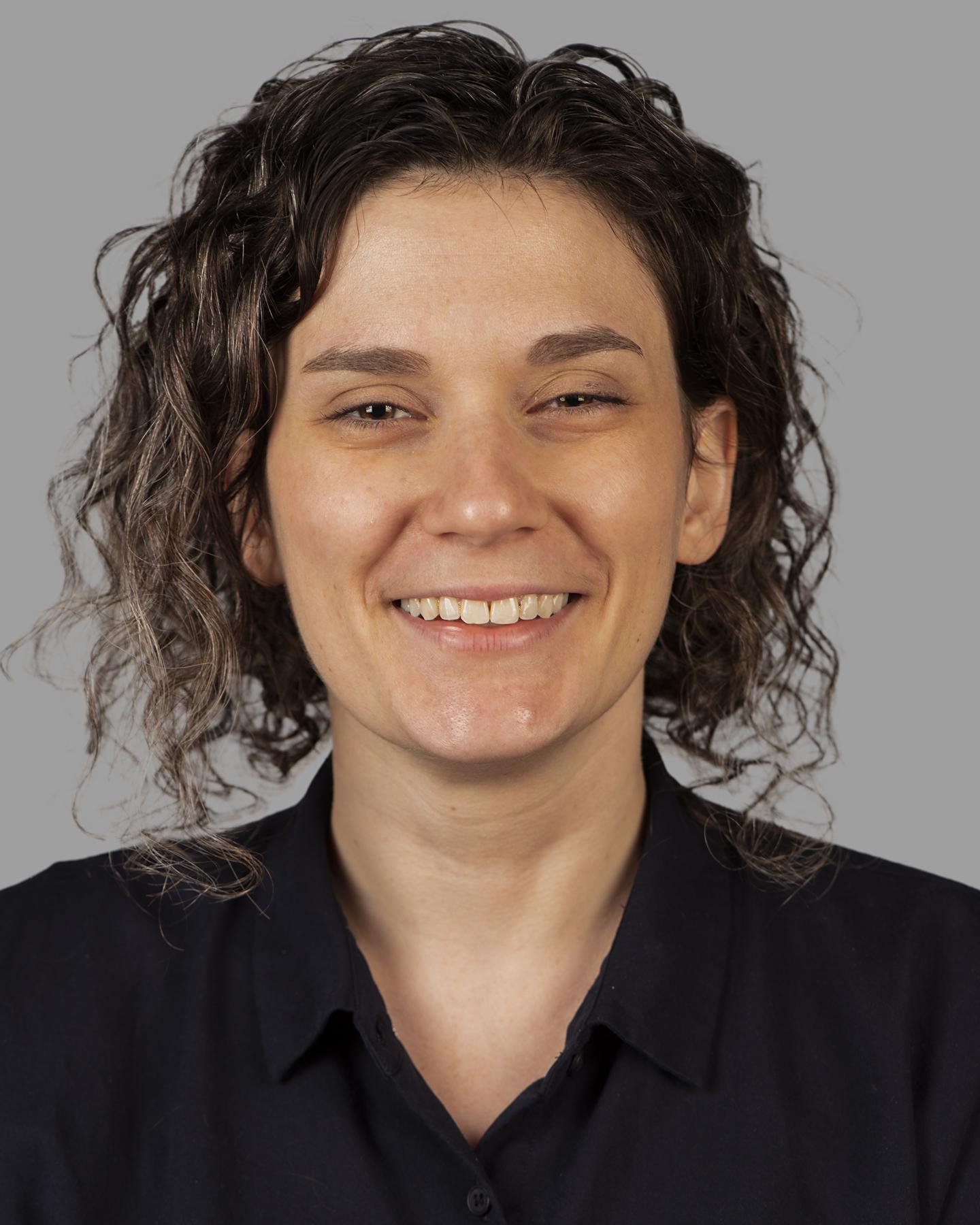 A white woman with short curly hair smiles at the camera 