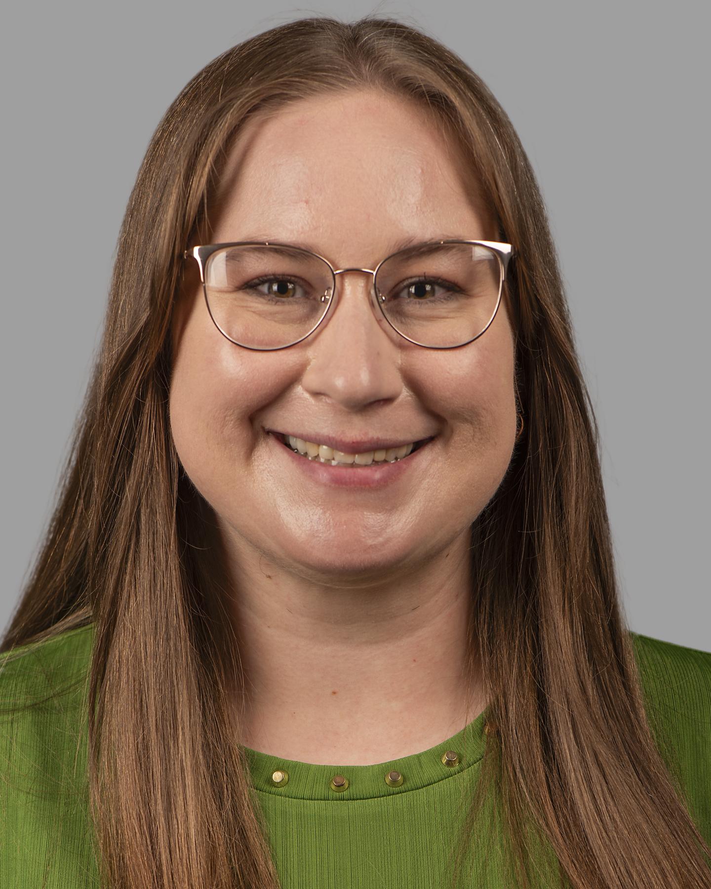 A white woman with long light brown hair wears gold framed glasses and smiles at the camera 