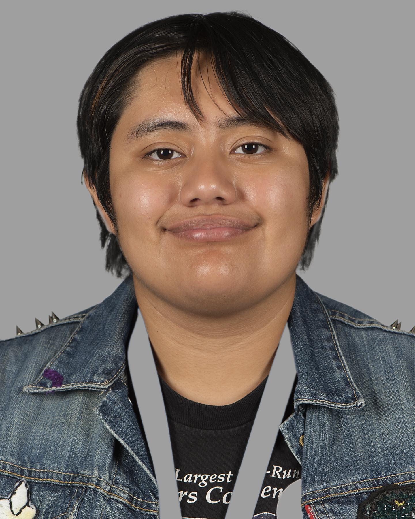 A brown-skinned man with black cropped hair wears a decorated denim jacket