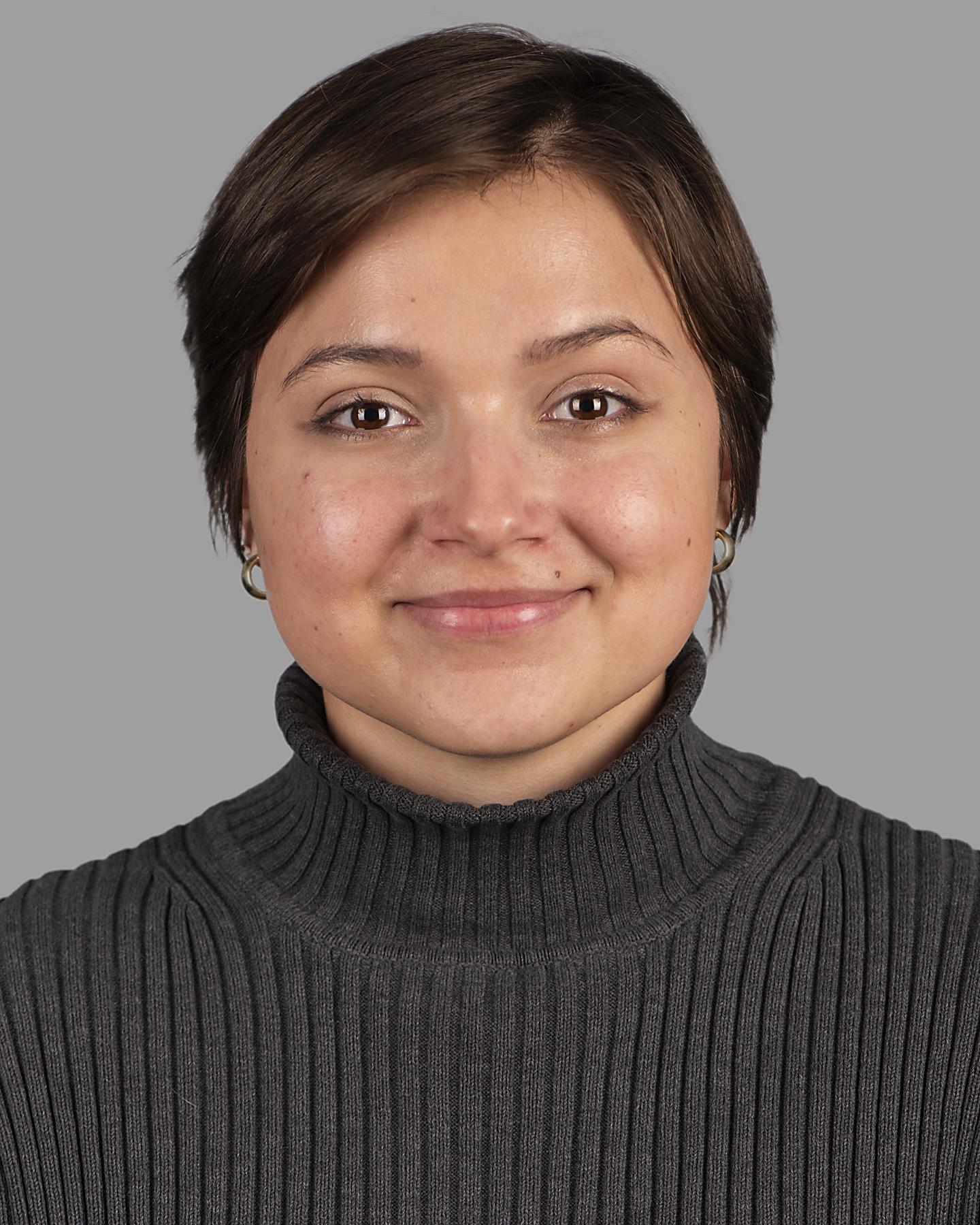 A woman with medium toned skin and cropped brown hair smiles at the camera