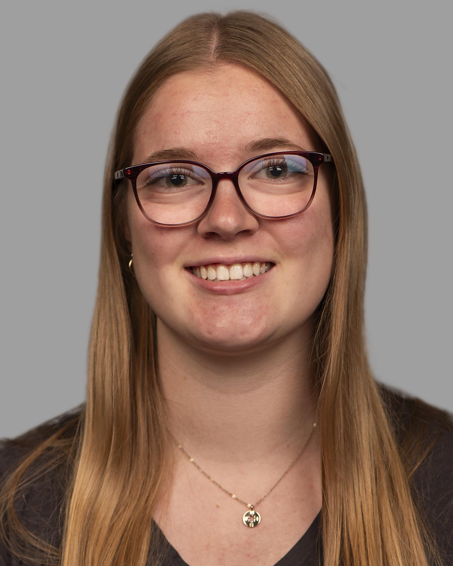 A white woman with long blonde hair wears square framed glasses and smiles at the camera