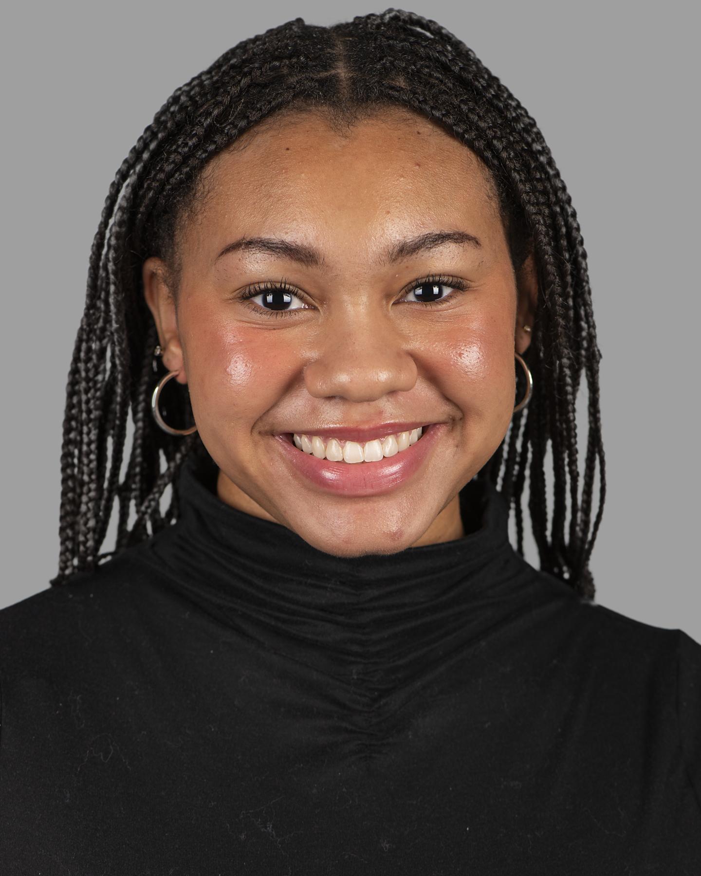 A Black woman with long black box braids wears silver hoop earrings and smiles at the camera