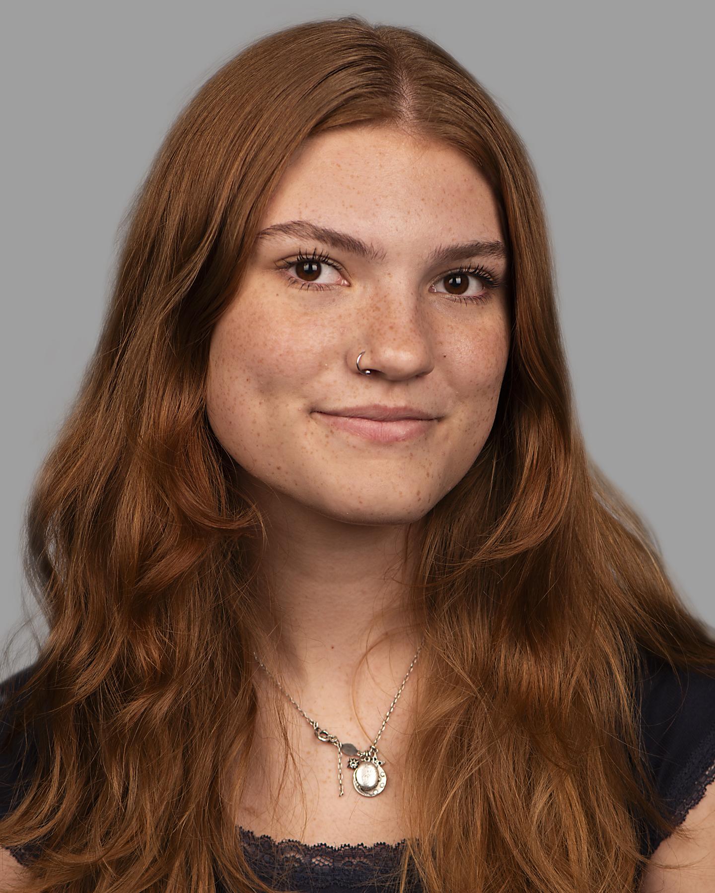 A white woman with long red hair and freckles smiles at the camera