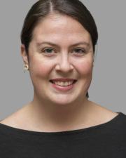 A white woman with tied back brown hair smiles at the camera