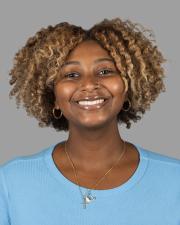 A Black woman has short light brown coily hair and wears a bright blue shirt; she smiles at the camera