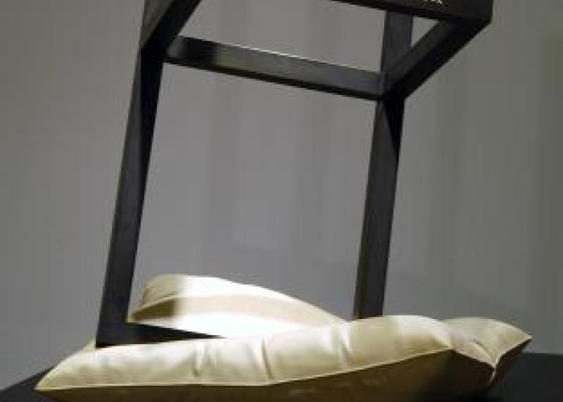 A sculpture of a metal chair frame balancing upside down on a pillow