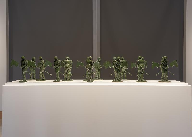 Green ceramic soldier figures ride hobby horses and are displayed in a group on a white pedestal