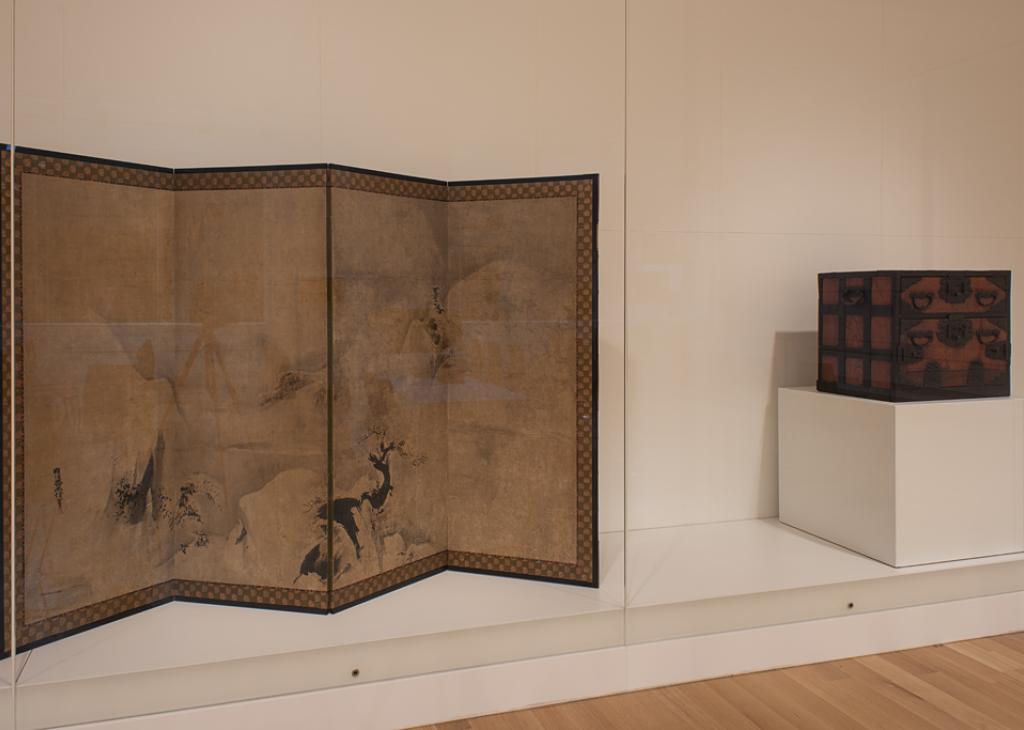 Photograph of a large glass case displaying a Japanese screen artwork and a wooden box next to each other 