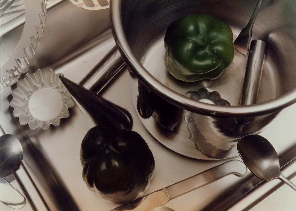 Photograph looking down on a kitchen surface with a green pepper in a stock pot and other tools