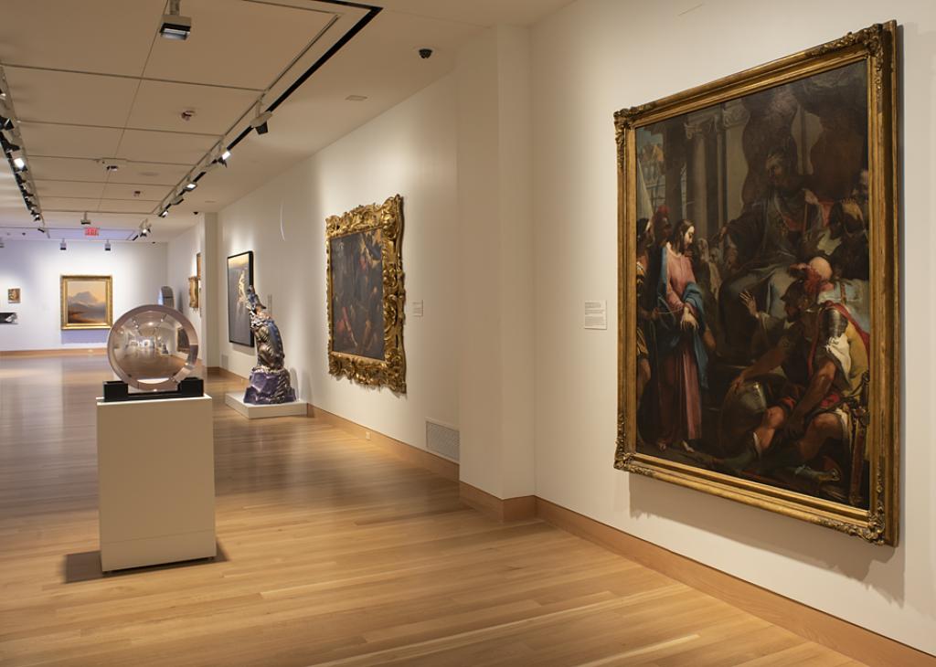 Photograph of a long museum gallery; large paintings hang on the walls 