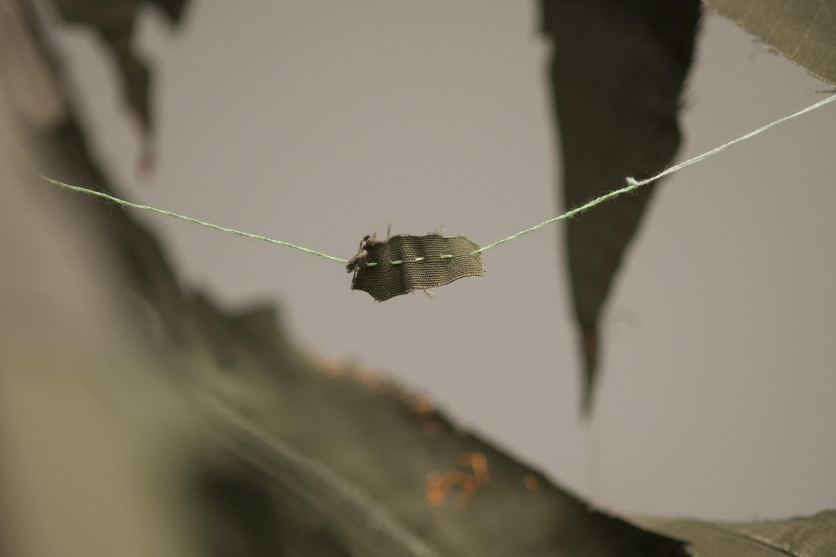Scraps of green fabric hang by multi-colored threads