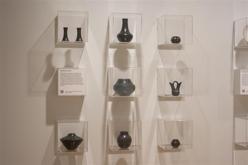 a three-by-three grid of glass cubes each holding blackware pottery