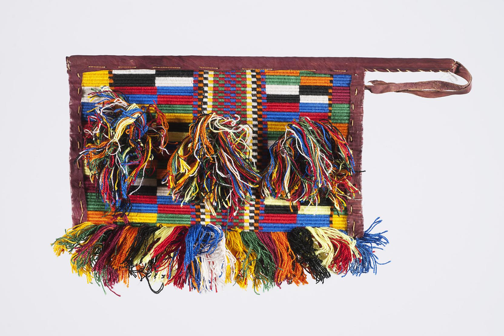 A multi-colored, rectangular woven artwork with a brown leather boarder and strap