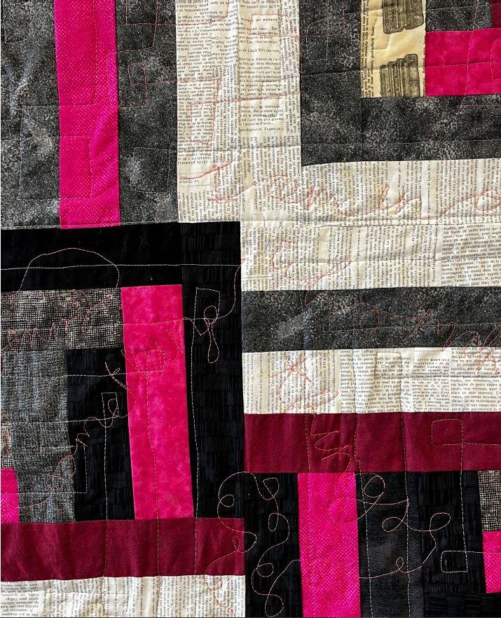 A quilt of black-, pink-, gray-, and cream-colored rectangles with words stitched on top using red thread