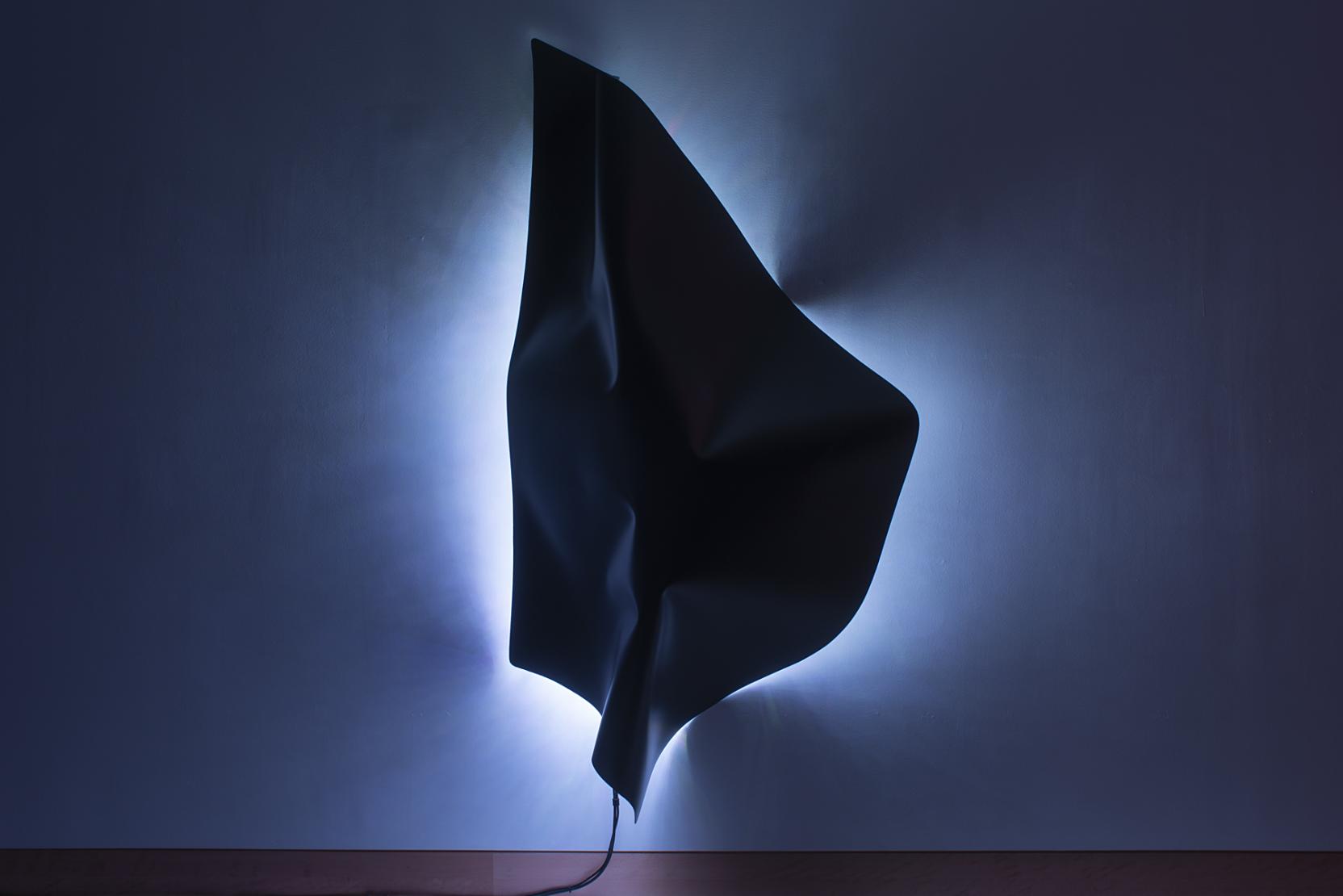 A dark abstract shape appears to hang on a wall with a glowing white light behind it