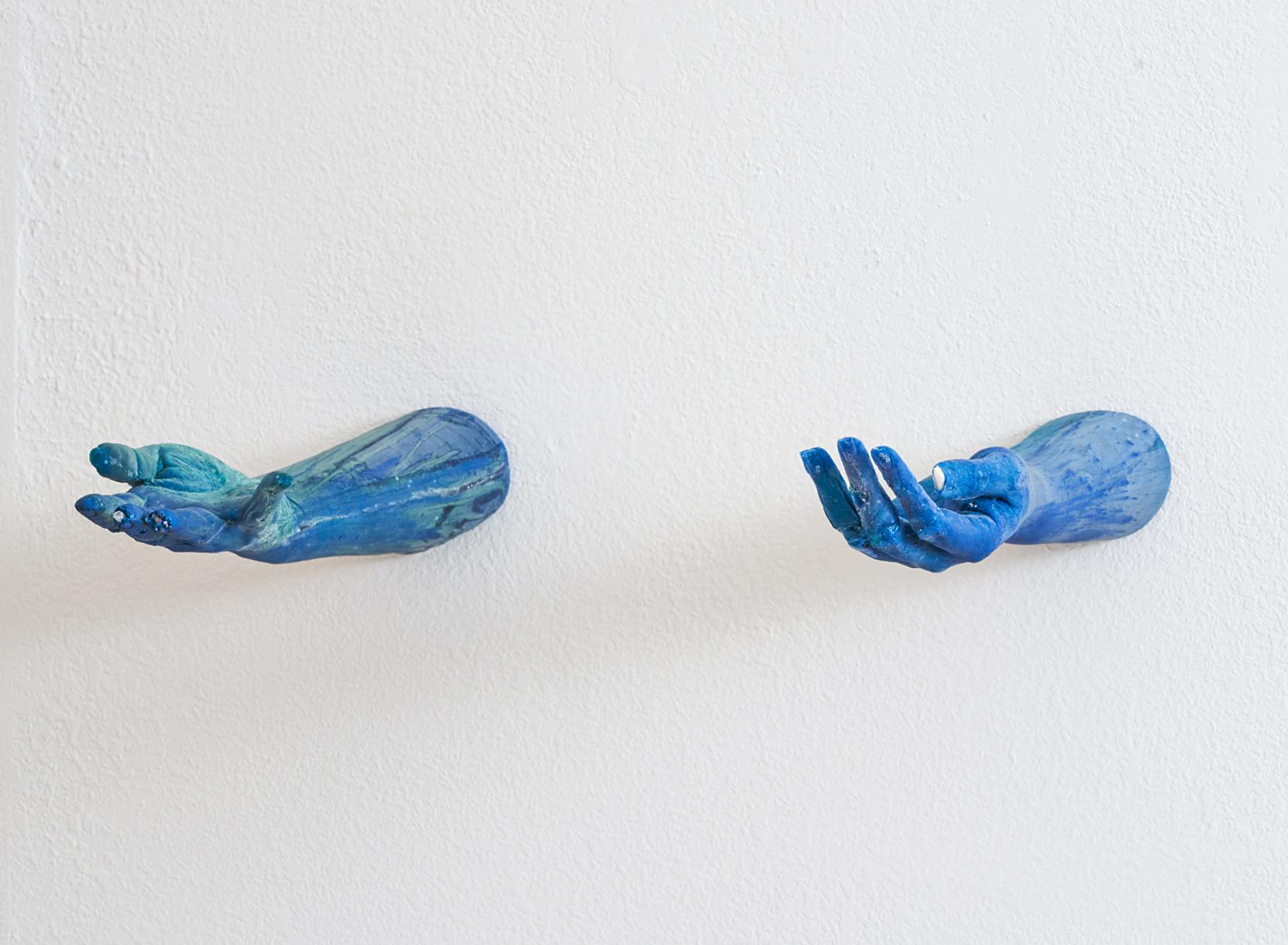 Two blue forearms with hands open stretched out from a white wall