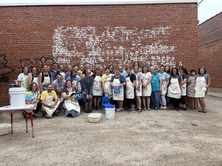 A group of adults wearing aprons pose in front of a brick building