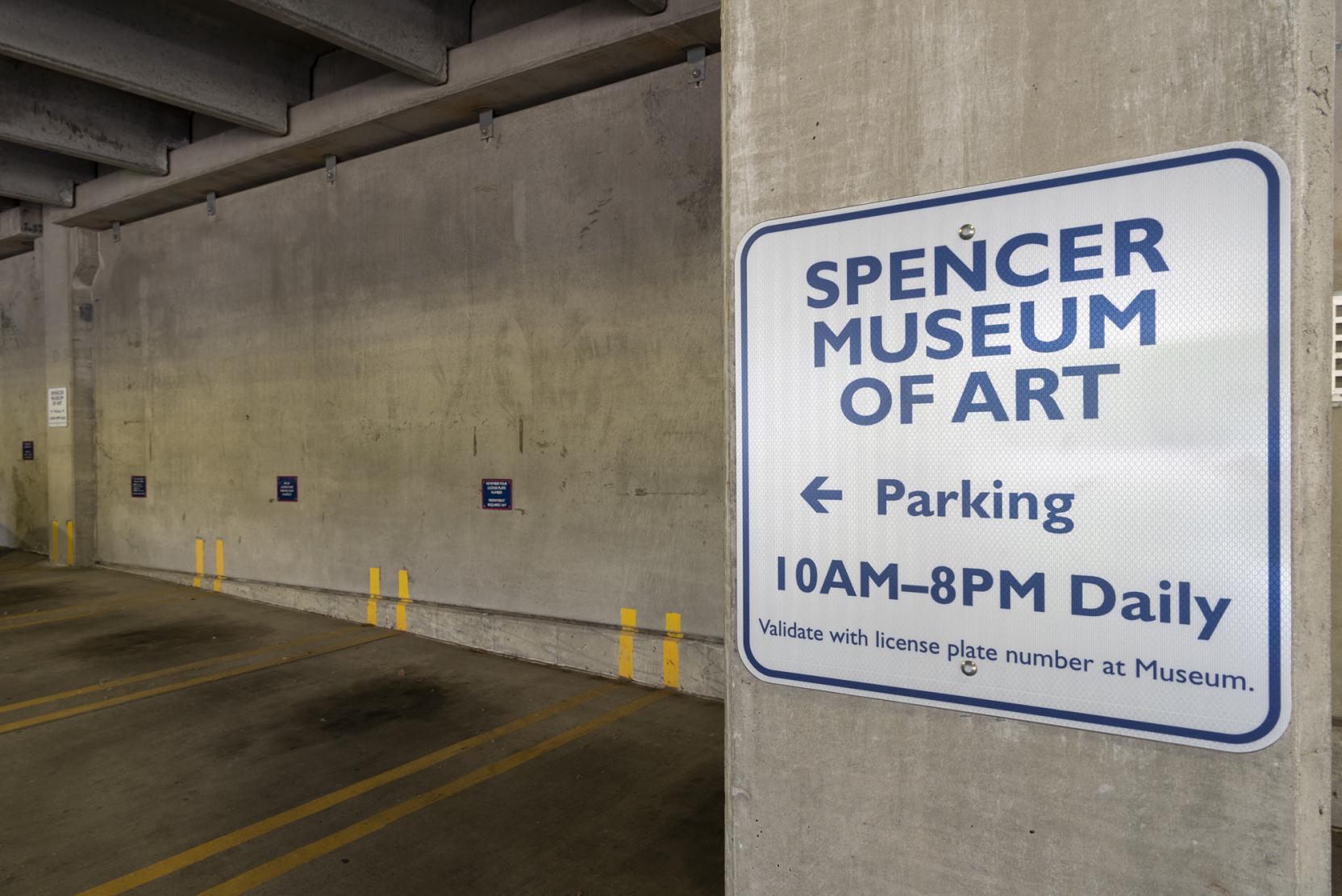 Photograph of a sign in a parking garage that reads “Spencer Museum of Art Parking, 10AM-8PM daily”