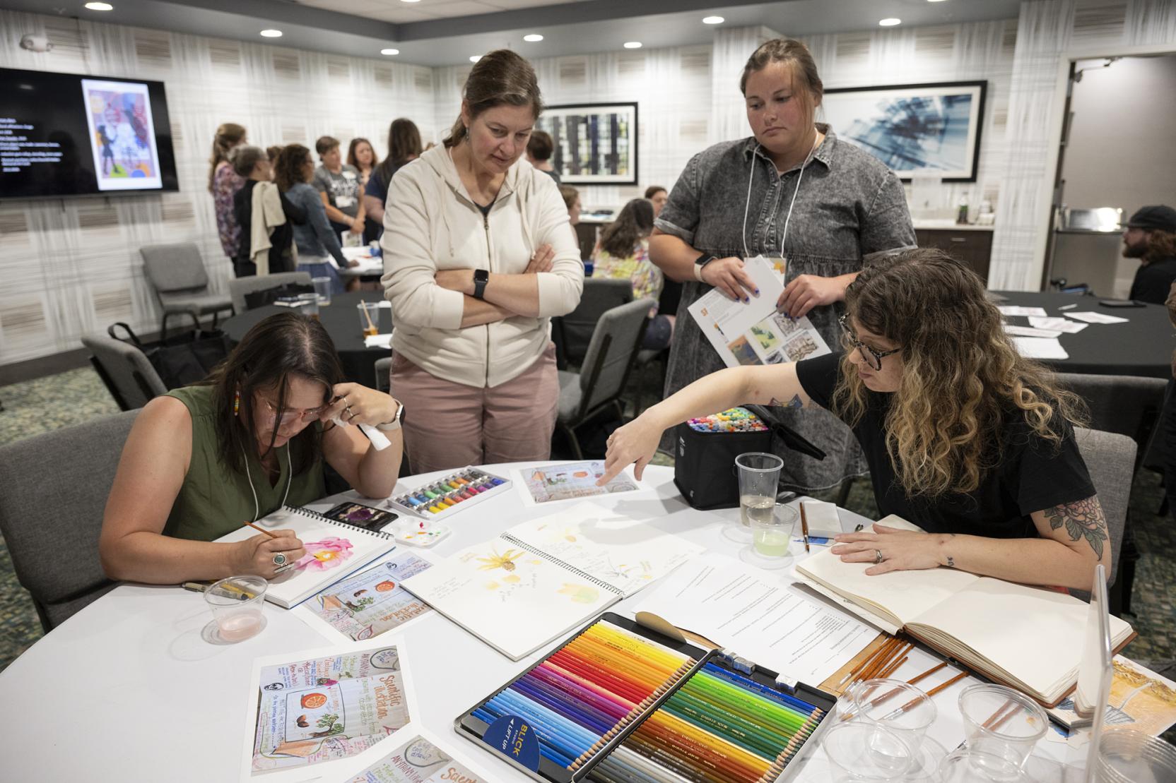 Four white women gather around a table with art supplies