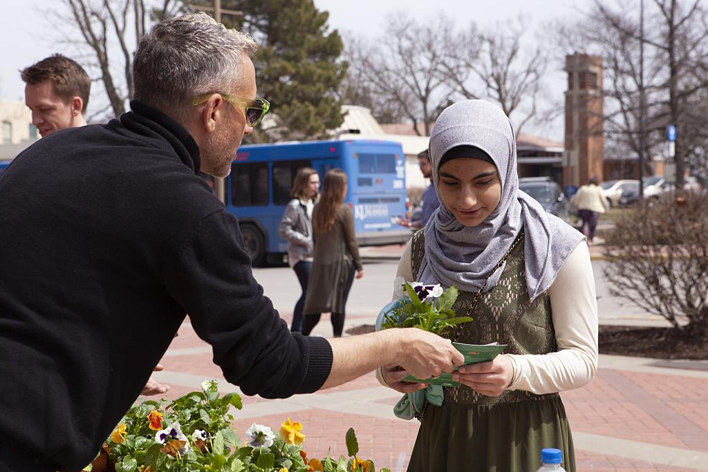 A white man with short gray hair hands a flower to a young woman wearing a gray headscarf