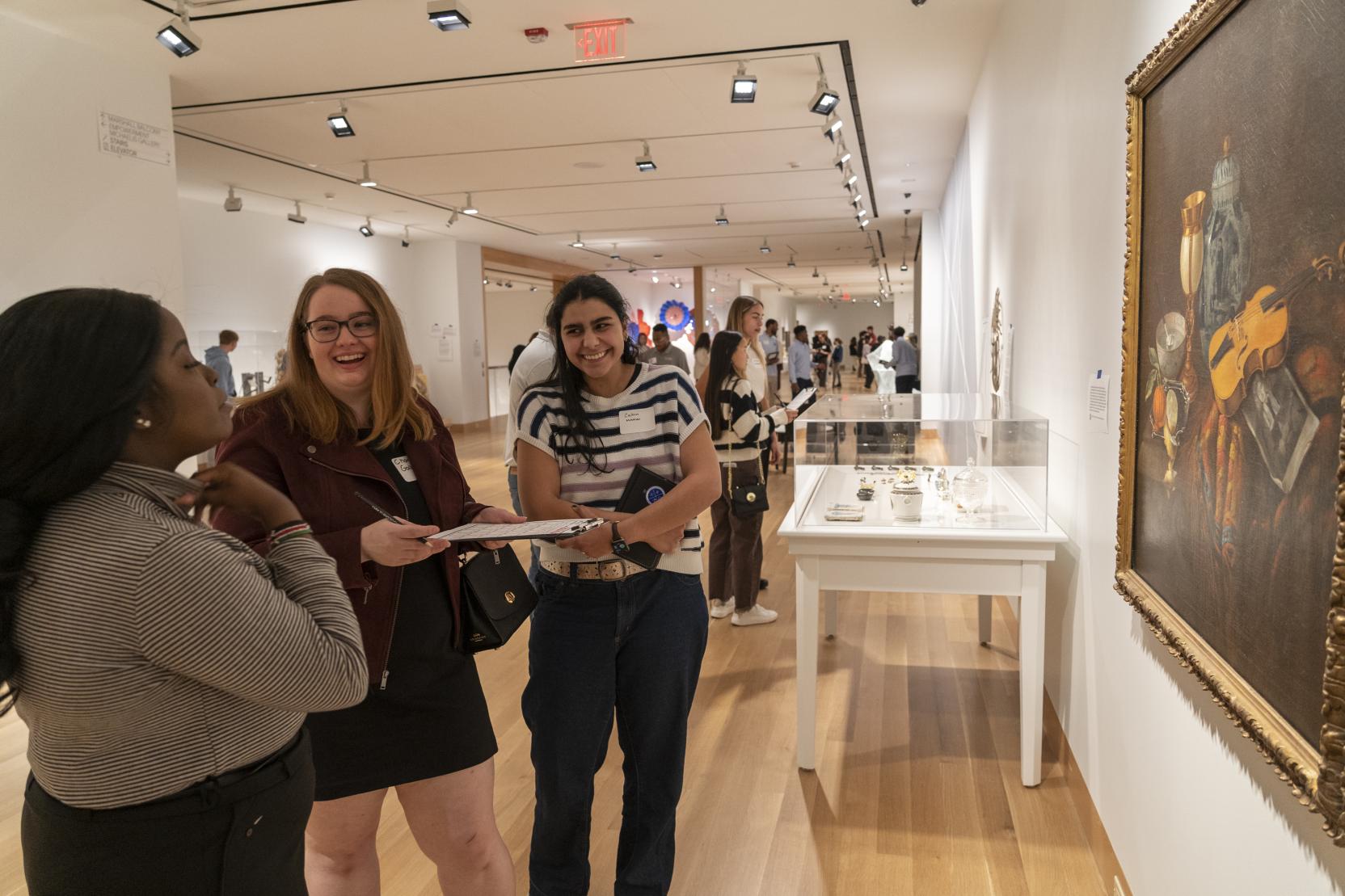 Three women stand in an art gallery and talk as they look at a painting in front of them