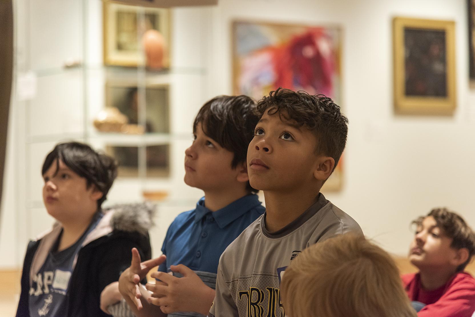 Photo of four boys sitting in an art gallery, they look forward at something outside of frame