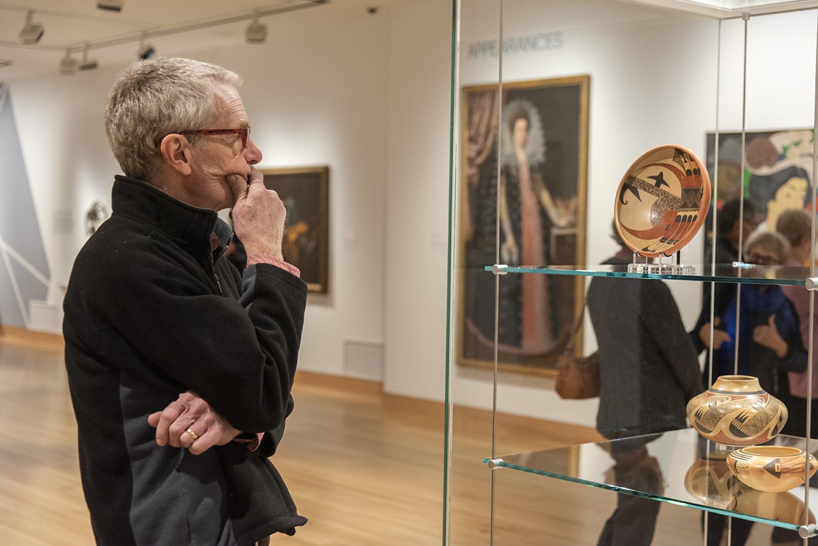 A white man wearing glasses stares at pottery displayed in a glass case