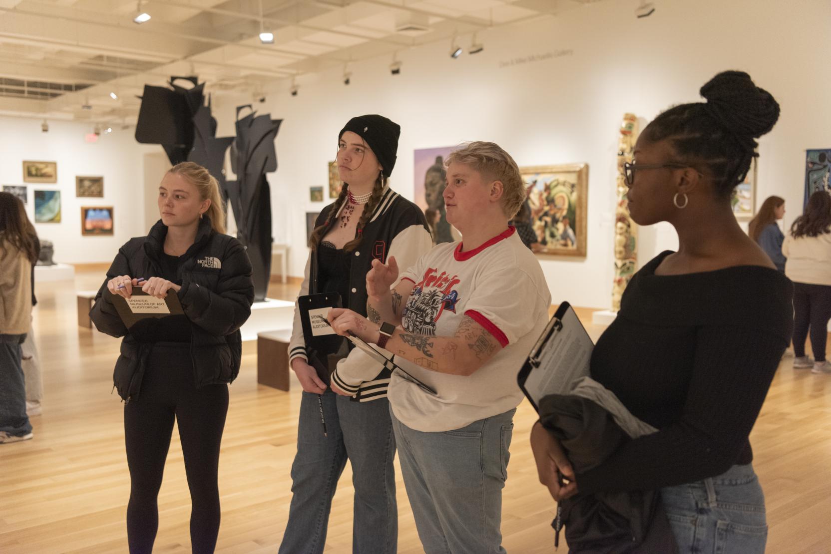 Four young adults dressed casually stand in a gallery space holding clipboards