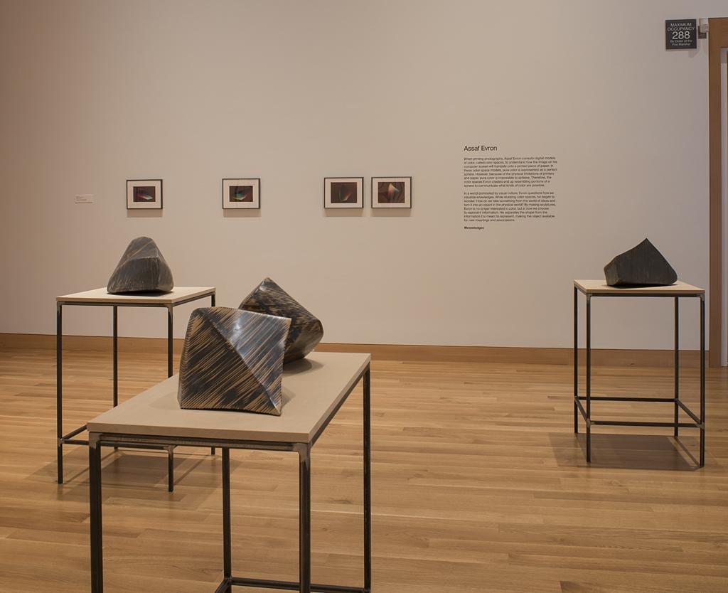Three tables in a wooden-floored gallery space hold four different abstract sculptures that look like large rocks