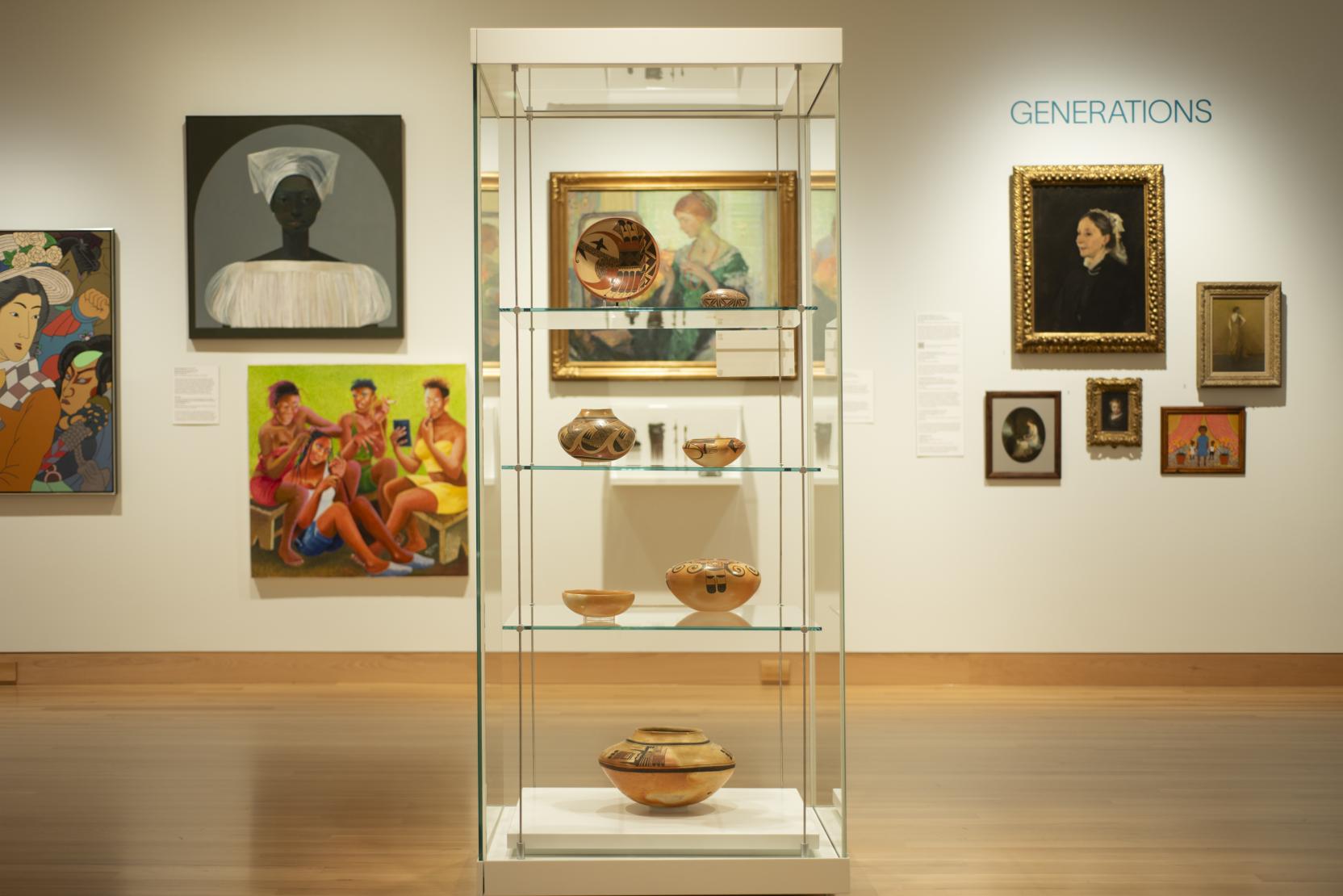 A glass case with four shelves displays potter in the center of an art gallery