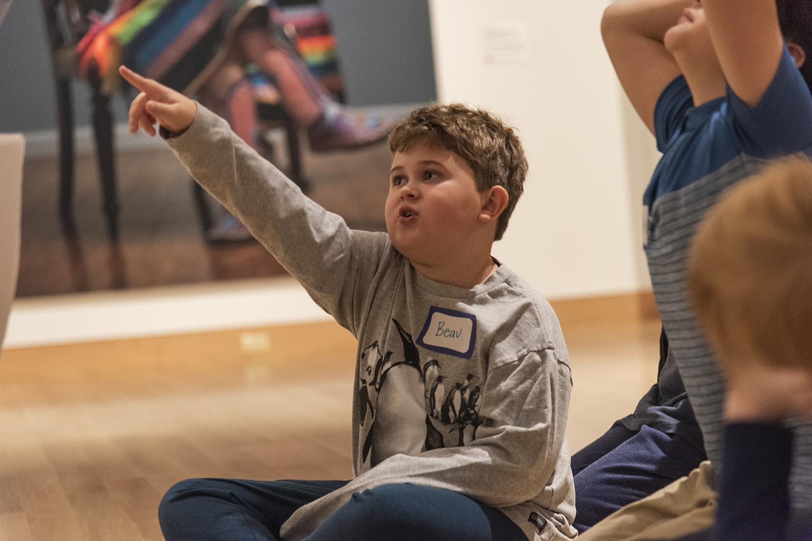 A photo of a boy sitting on the floor of an art gallery and pointing toward something out of frame