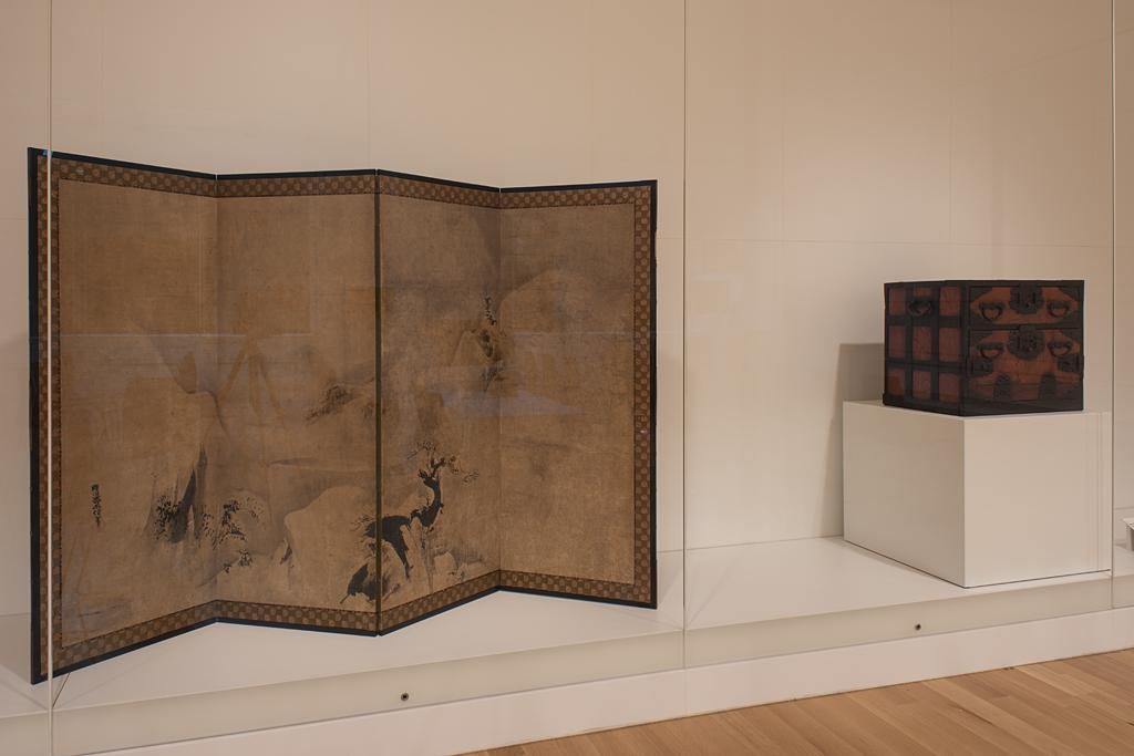 Photograph of a large glass case displaying a Japanese screen artwork and a wooden box next to each other