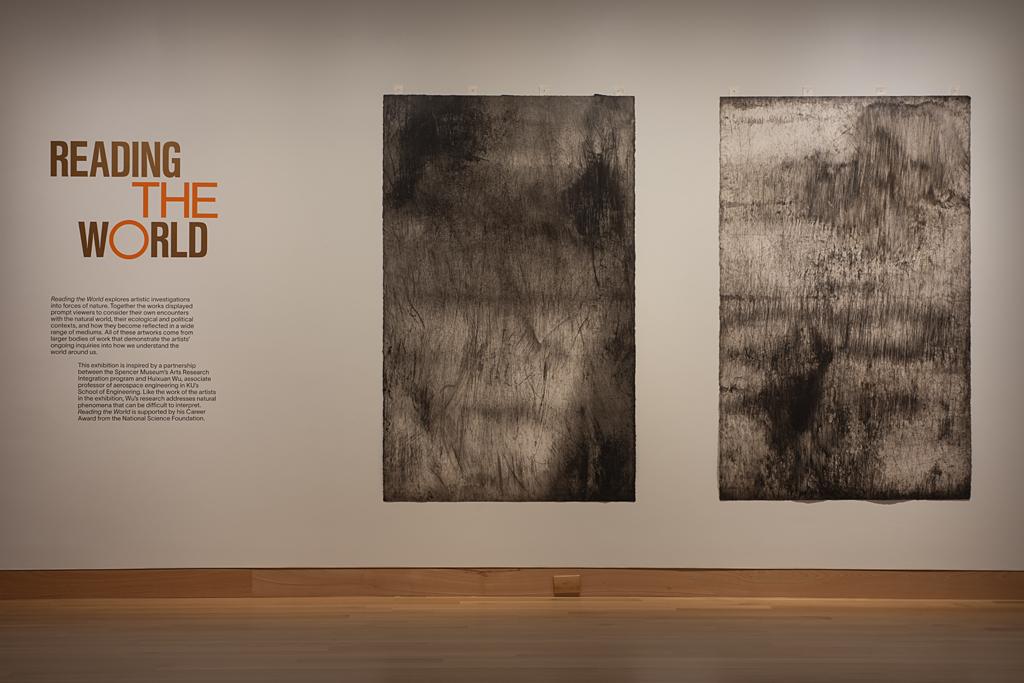 Gallery wall featuring the words "reading the world" in red; two large rectangular canvases hang to the left of the words