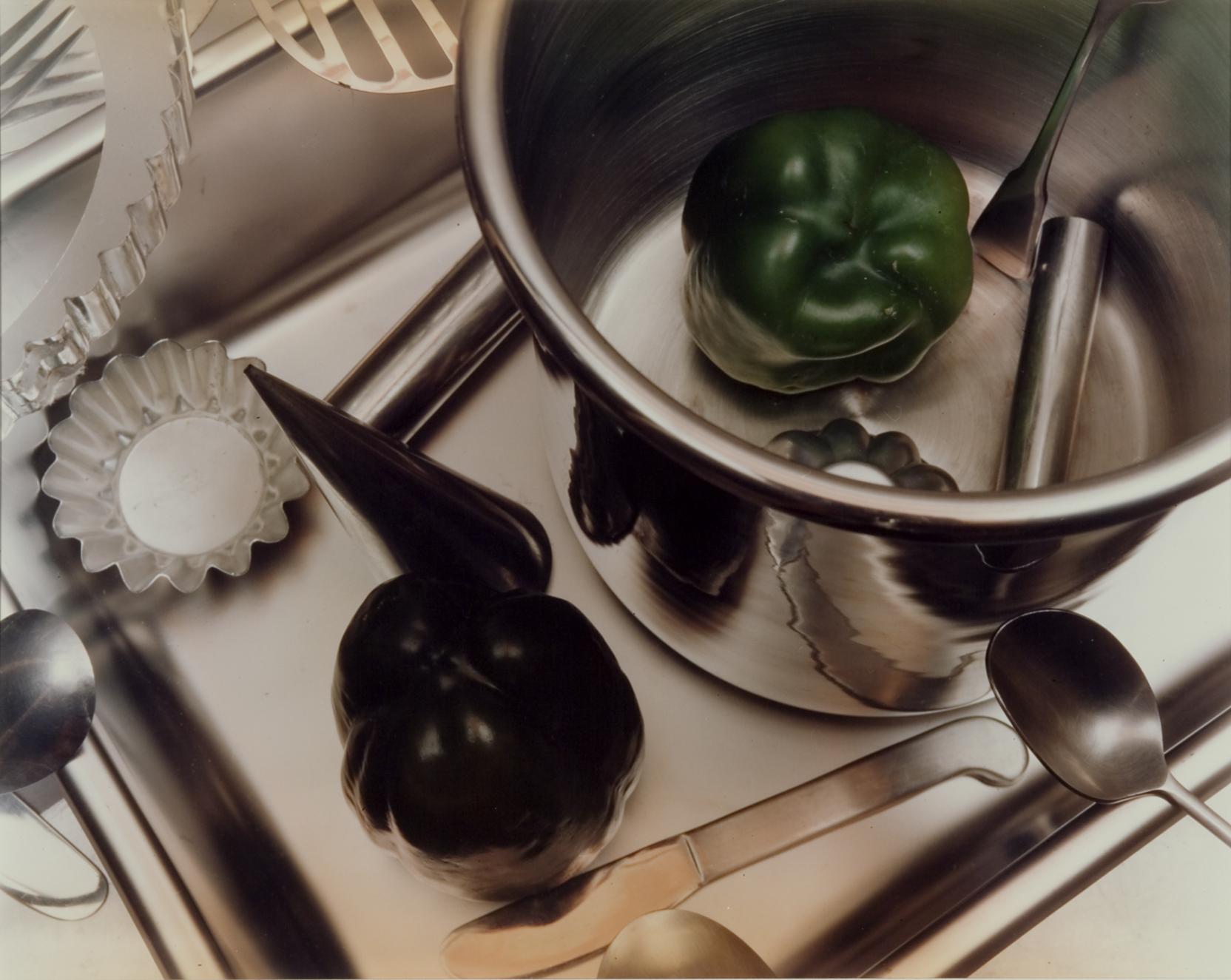 Photograph looking down on a kitchen surface with a green pepper in a stock pot and other tools