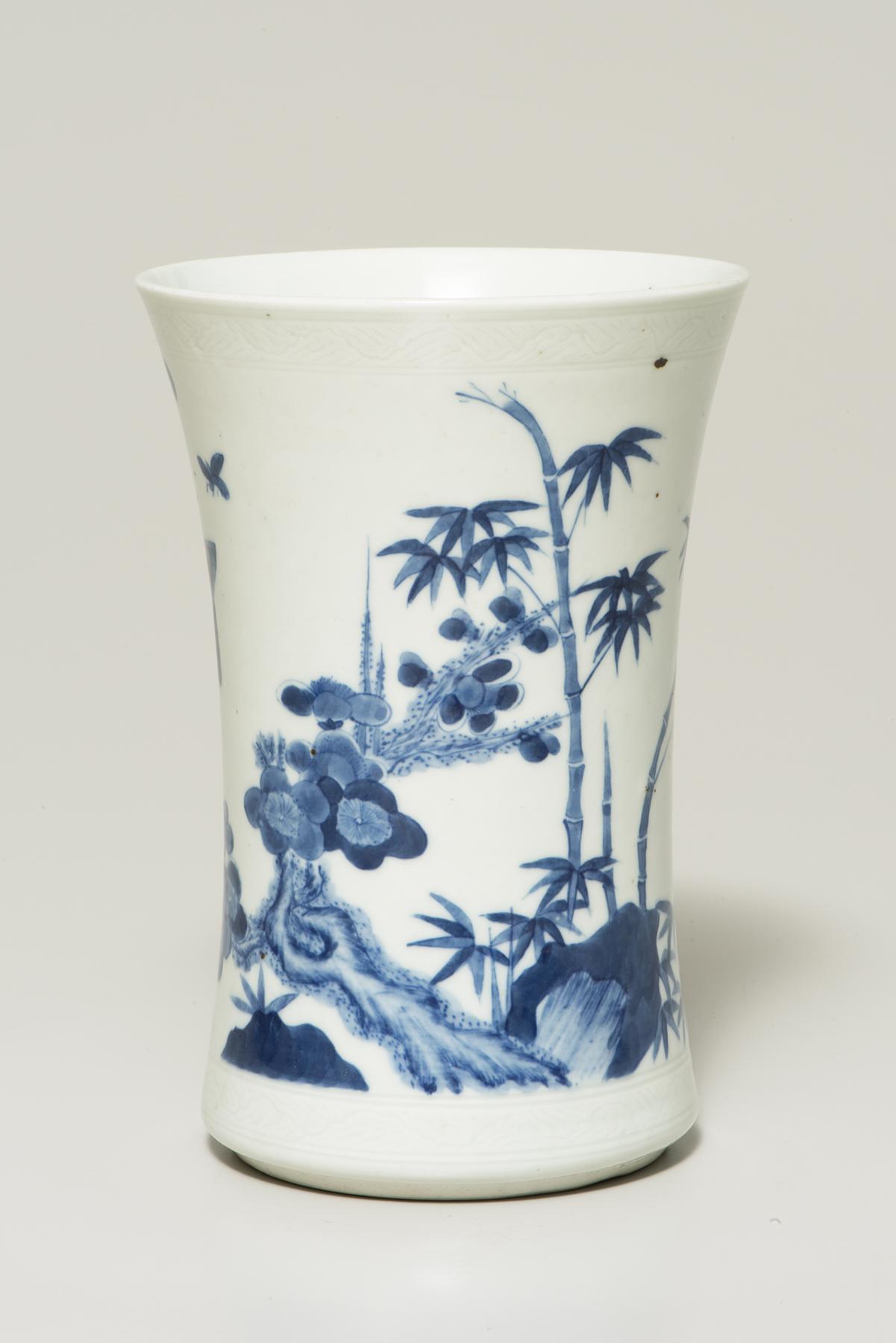 A tall white ceramic pot with bamboo, tress, and flowers painted on it in blue