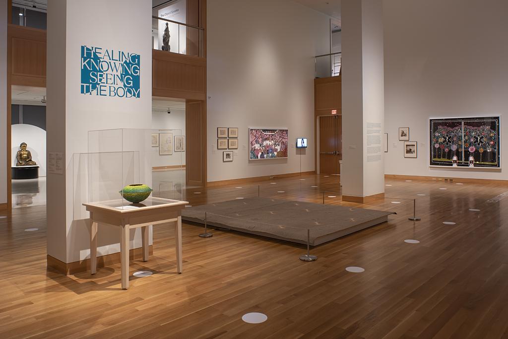 Photograph of an art gallery; artwork and text appear on the walls and the two columns in the center of the room 
