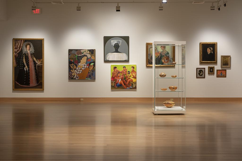 Art gallery with wood floors and white walls displaying bright paintings of women through the centuries